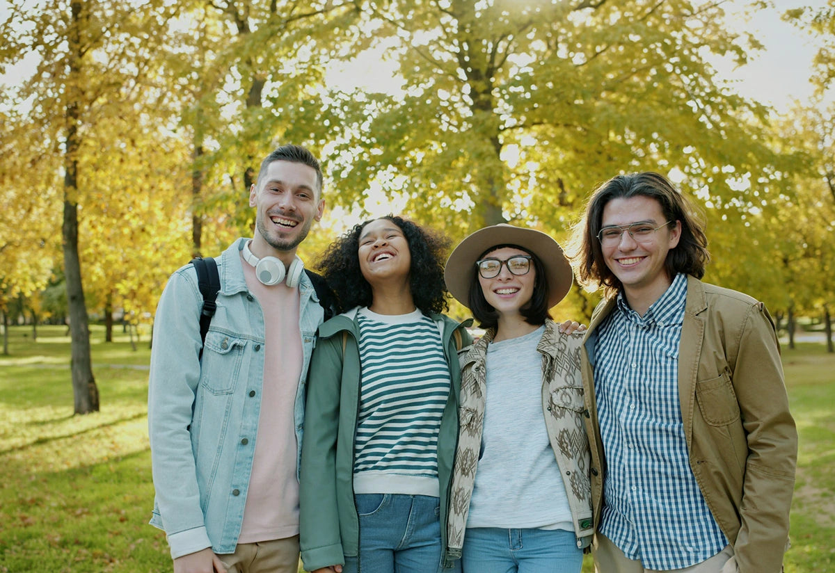 A group of four young adults smiling, standing side by side outside. 