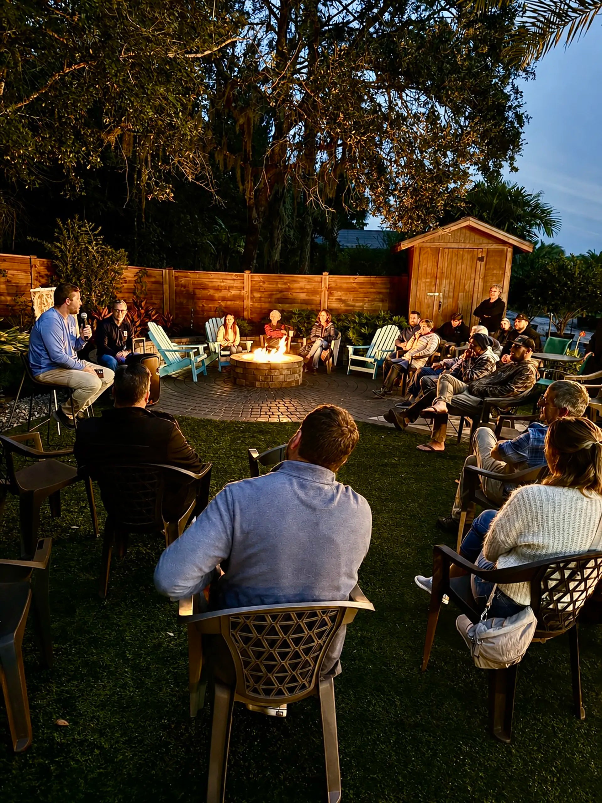 Group of people gathered around a fire pit in a backyard setting